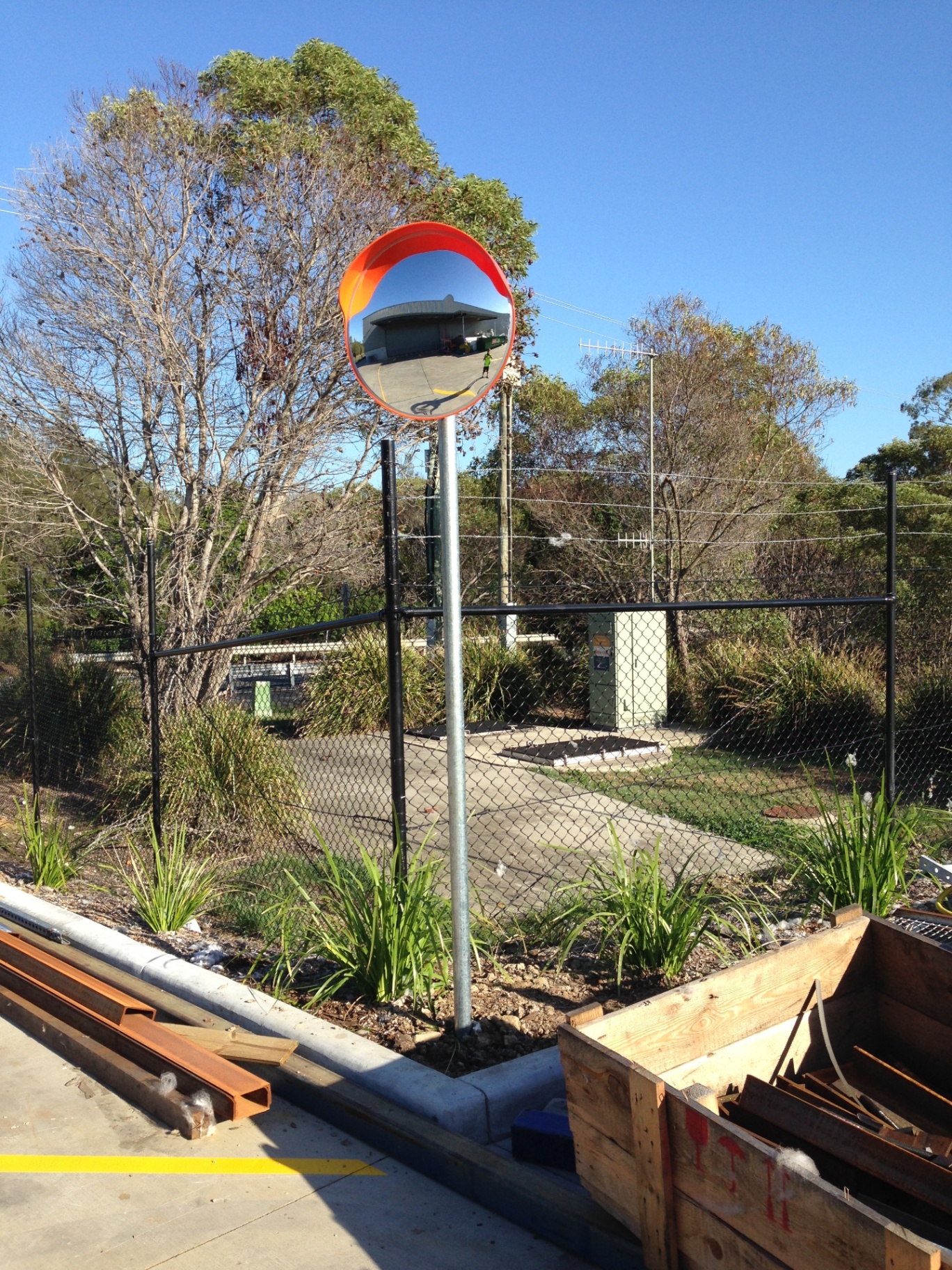 Orange convex safety mirror installed on galvanised pole at industrial site