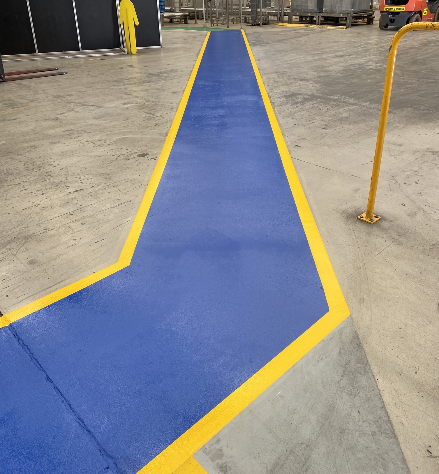 Blue pedestrian walkway with yellow safety border in industrial facility