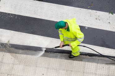 Worker cleaning a street sidewalk with high pressure water jet. Public maintenance
